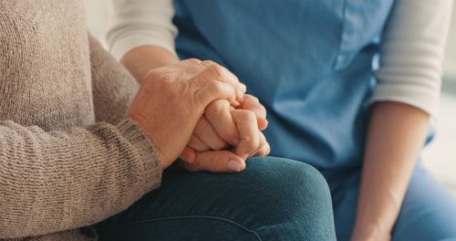 Cropped shot of a nurse and senior woman holding hands - wrongful death lawsuit concept