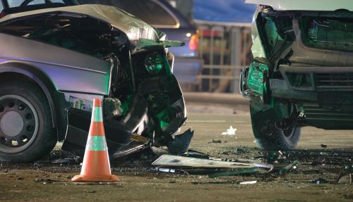Damaged vehicles after collision on city street crash site at night - after a car accident concept