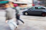 Abstract blurred image of a walking couple and driving car on a city street. Visual concept for a personal injury blog discussing Comparative Negligence Laws in Washington State.