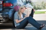 Woman has hit her head on the steering wheel during a collision and the rear bumper of her car is crushed in. She sits in shock waiting on help and law enforcement to arrive. Visual concept for personal injury blog discussing minor car accident injury.