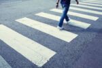 Man in jeans walking across a pedestrian crosswalk.