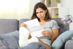 Worried woman with a worker injury reading a workers compensation appeal denial letter while sitting on a couch in the living room at home.